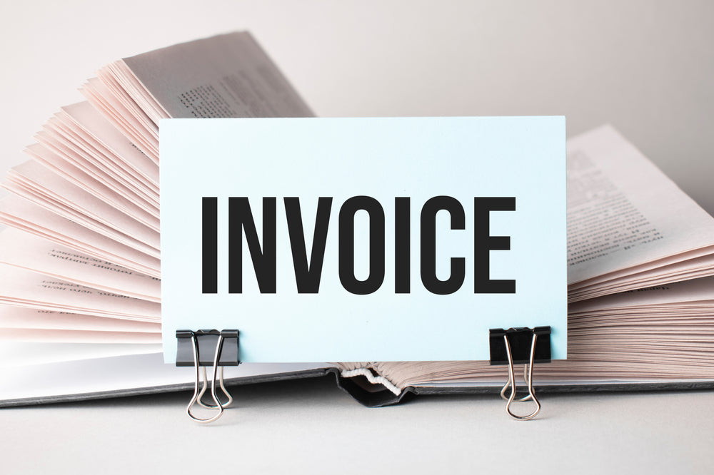 An open book with a card labeled "INVOICE" clipped to the pages, symbolizing financial documents or billing processes.
