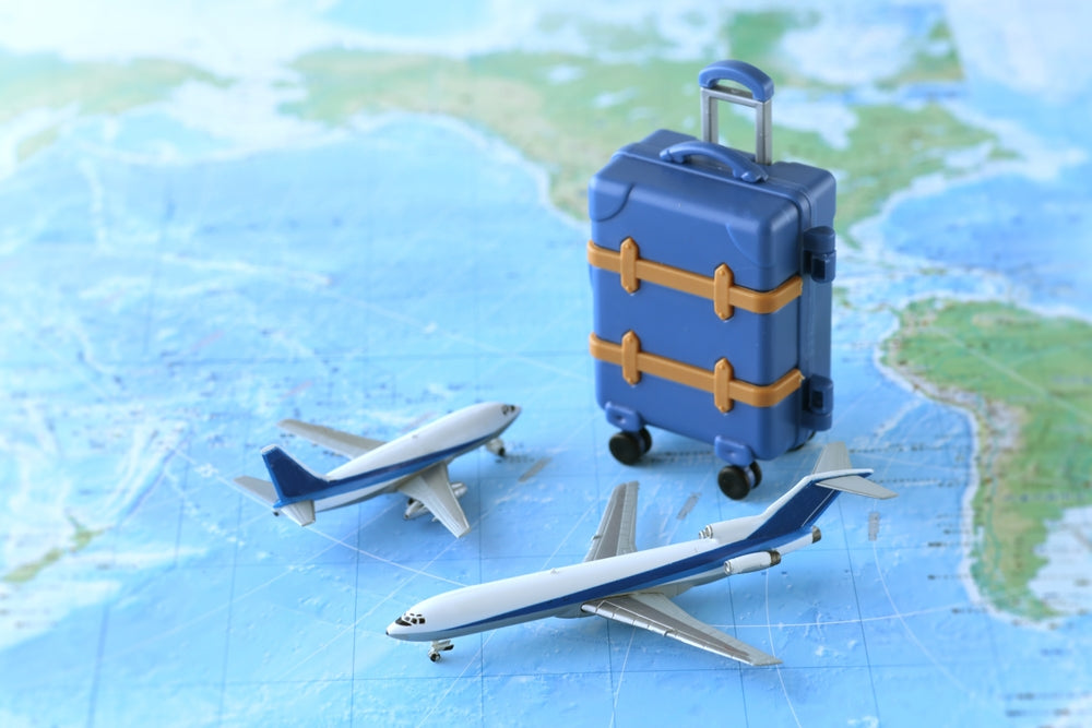 A toy suitcase and miniature airplanes placed on a world map, representing travel, aviation, or international tourism.