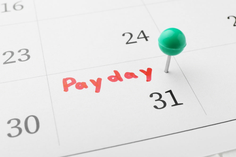 Calendar with the word 'Payday' written in red on the 31st, marked with a green pushpin, symbolizing salary day.